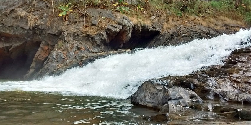 A towering granite monolith with deep hollows, set against the backdrop of the Kaneri River in Dandeli National Park.