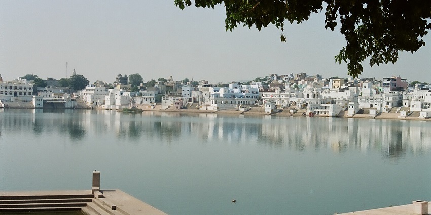 A view of Pushkar Lake in Rajasthan with its calm waters reflecting the buildings.