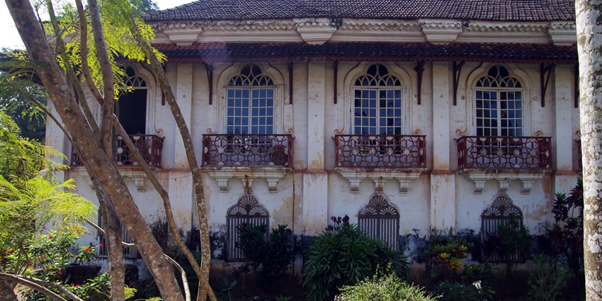 A picture of the stunning Menezes Braganza House in Goa with flowers blooming in its garden area