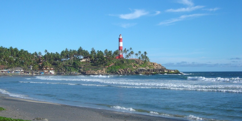 Image of lighthouse near the beach surrounded by lush greenery and tranquil water