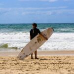 Stunning view of a water body with a man in front holding a surfing board during the day.