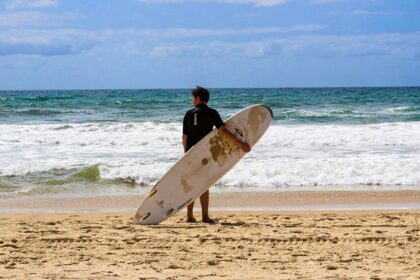 Stunning view of a water body with a man in front holding a surfing board during the day.