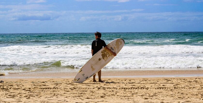 Stunning view of a water body with a man in front holding a surfing board during the day.