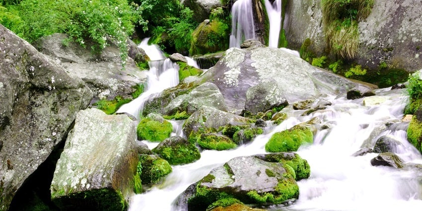 Image of Jogini waterfall cascading through rocks and surrounded by lush greenery.