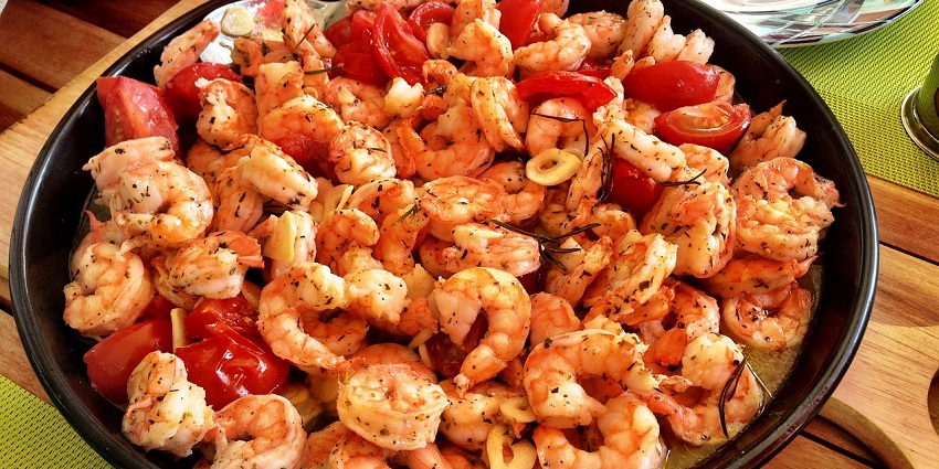 A round dish of shrimp in sauce, garnished with green chili peppers and parsley