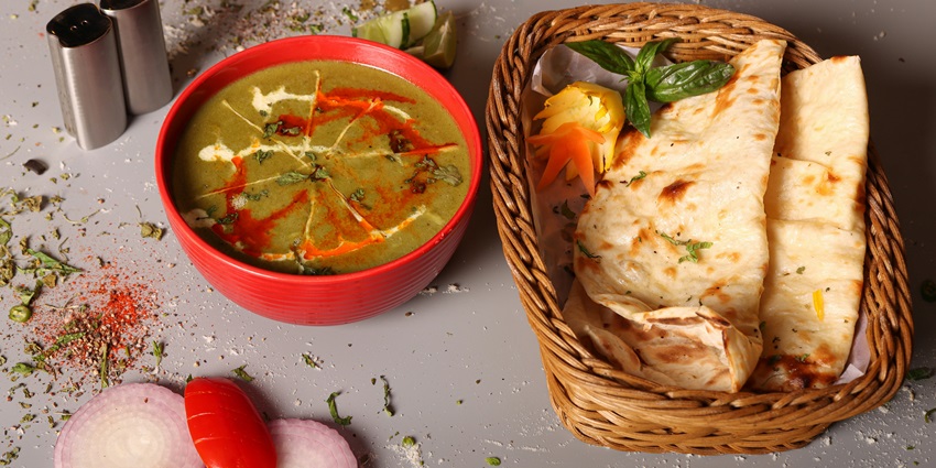 A mouth-watering view of a bowl served with a green curry and flatbreads on the side.