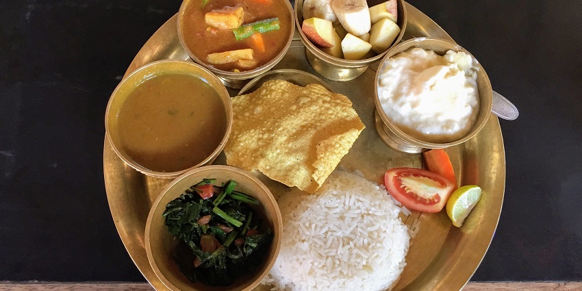 A mouth-watering view of a traditional Nepali thali with cooked vegetables and rice.