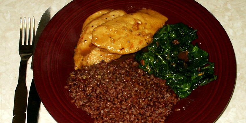 A traditional Bhutanese meal of red rice, chicken, and spinach, reflecting the local cuisine around the Karbandi Monastery.