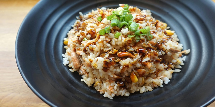 A mouth-watering view of a black ceramic plate served with cooked rice and greens.