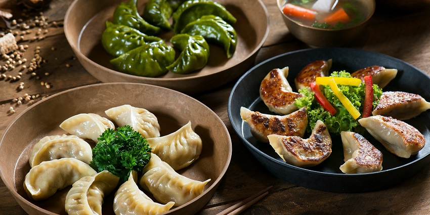 A mouth-watering view of a plate of assorted momos served with different dips and greens.