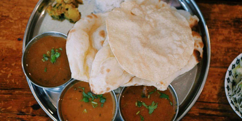 Image of Indian food served on a plate with papad, curry, rice and side dishes