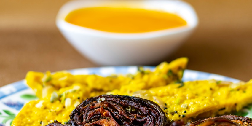 A mouth-watering view of a white plate served with Patra and Khandvi with a dip on side.