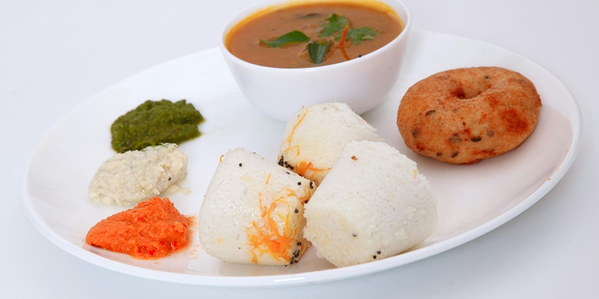 White ceramic bowl with rice and a flavorful meat dish, garnished with fresh greens