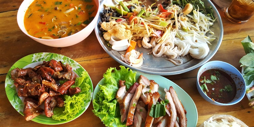 A tempting view of a table served with different Thai food, pasta and meat for all.