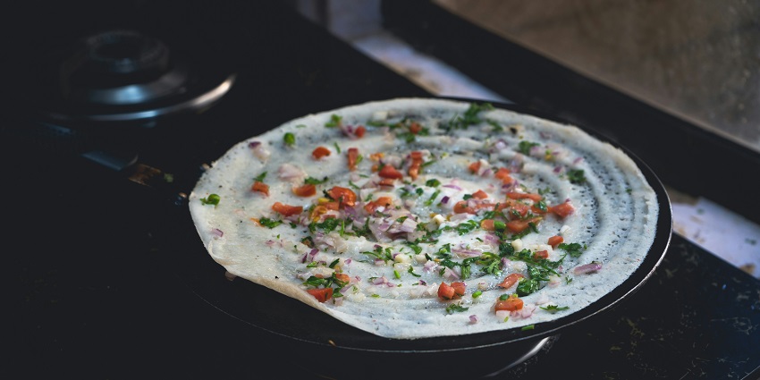 A mouth-watering view of a pan with a dosa cooking on it garnished with vegetables.