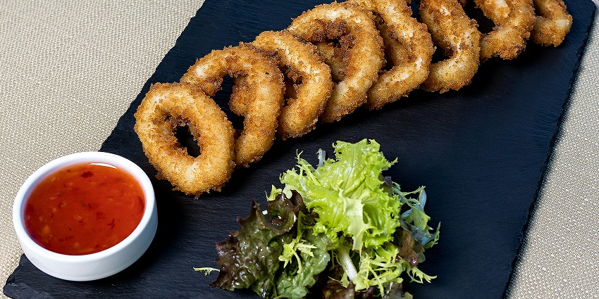 A black plate with Chicken Rings, nuggets, and calamari with tomato sauce served on it.