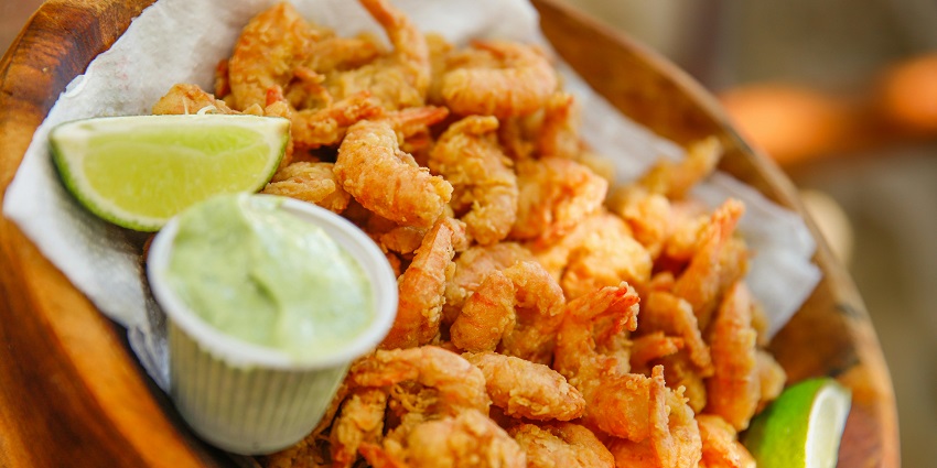 A white ceramic plate holds shrimp, French fries, and colorful vegetables