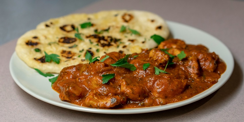Image of delicious roti and chicken curry with coriander on top served on a white plate