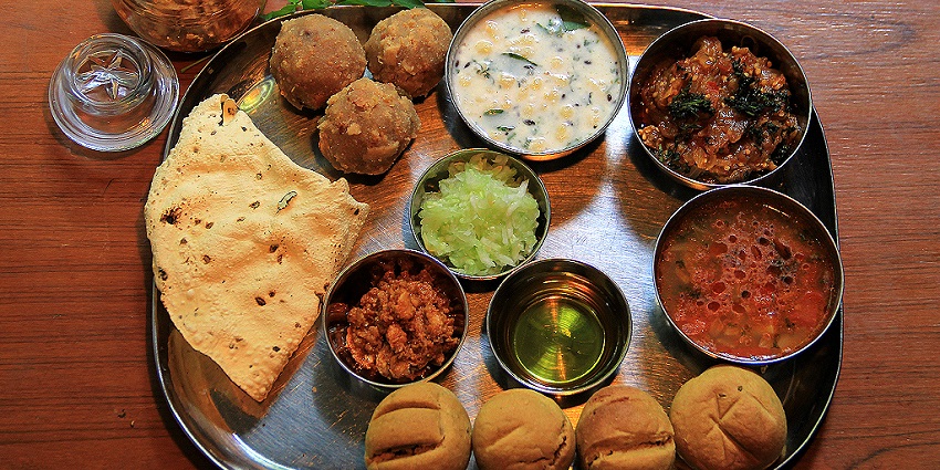 A mouth-watering view of a thali served with different cooked vegetables with sides.