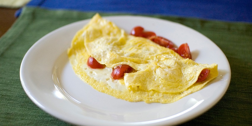A white plate with a fluffy omelet and a fresh salad on the side for a healthy breakfast.