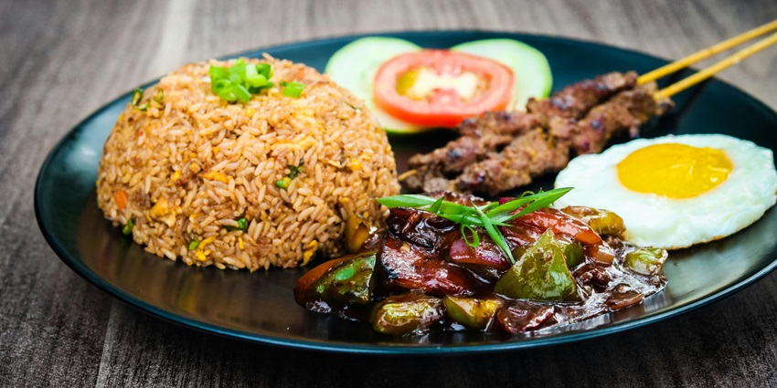 Close-up of a Nasi Goreng dish served with a fried egg, prawns, and fresh vegetables.