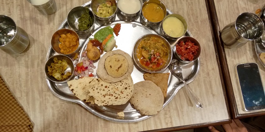 A traditional Madhya Pradesh thali featuring a variety of dishes served on a metal plate.