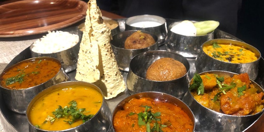 A variety of traditional Rajasthani dishes served on a platter, including curries, bread, and rice.