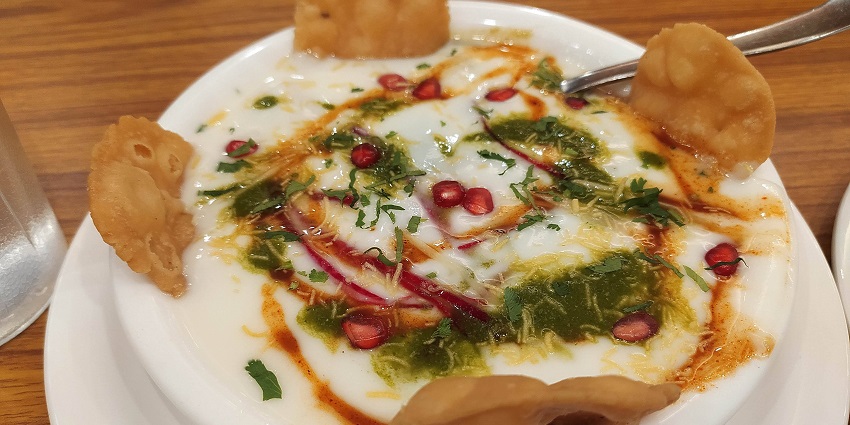 Papdi Chaat made from curd, papdi, tamarind chutney, green chutney and garnished with namkeen and fruits such as pomegranate.