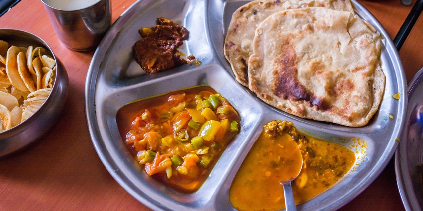 Image of Indian meal cooked and served on a round plate with different sections