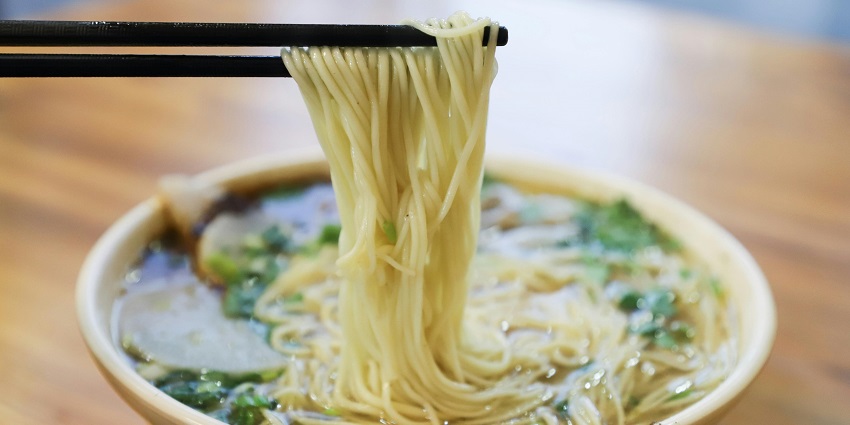 An image showing delicious cooked noodles on a bowl and vegetables with the soup