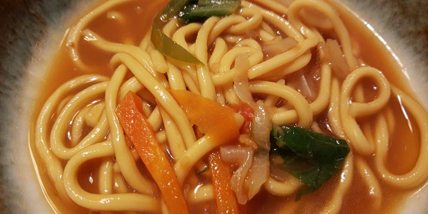 A bowl of Thukpa, a traditional Tibetan noodle soup with warm vegetables and herbs.