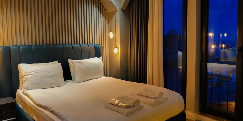 Image of a guesthouse room with dim lights bed, pillows and towels on the bed