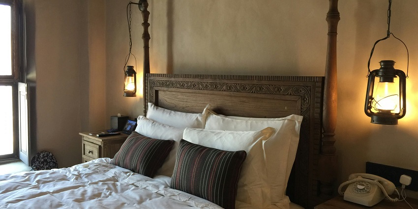 A picture of a hotel room with a brown wooden bed, pillows, two lanterns, and a telephone.