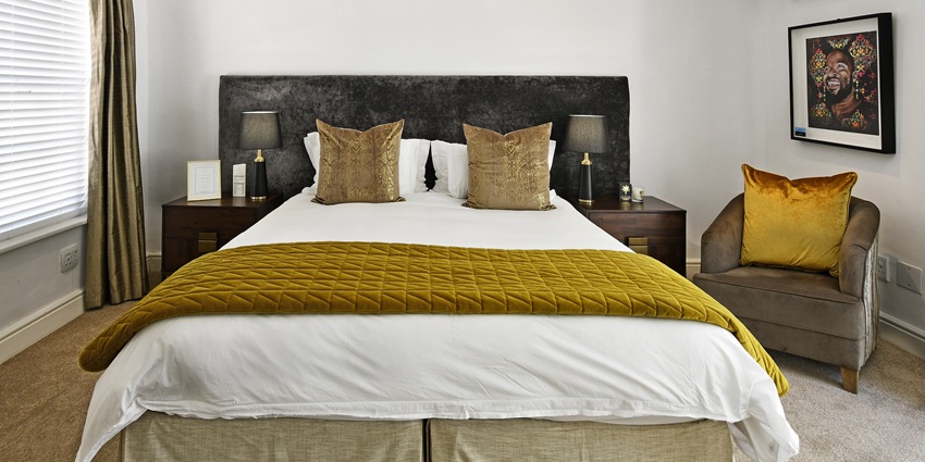 Image of a hotel room with bed, pillows and clean sheets and sofa on the side