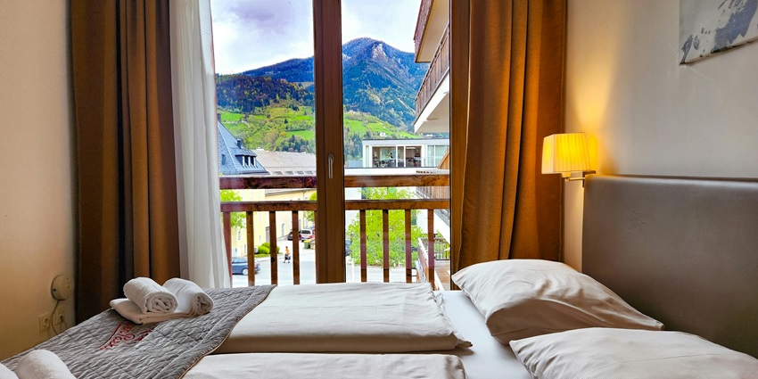 A cosy bedroom in a hotel with a beautiful view of the mountains from the windows.