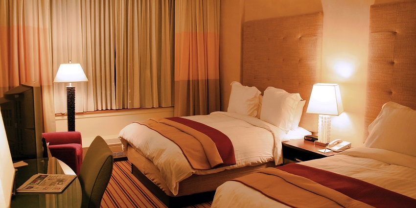 A luxury hotel room with two medium-sized beds and multiple types of dim lights glowing.