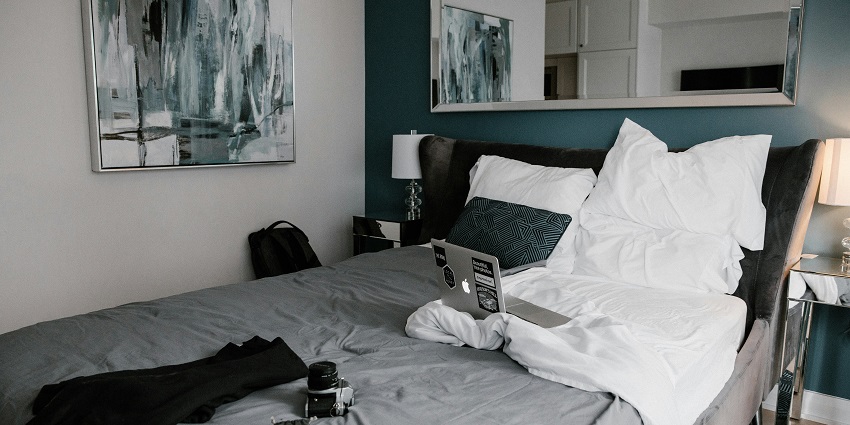 Image of a hotel room with a bed, pillows, lights and other essentials and clean sheets
