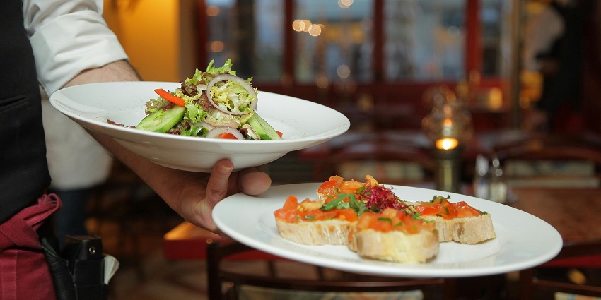 A person holding a pastry and the onion salad on the ceramic plate, which is being served