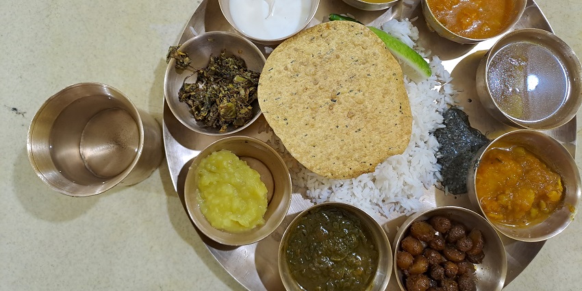 A lip-smacking view of a thali served with Assamese food and a glass of water on the side.