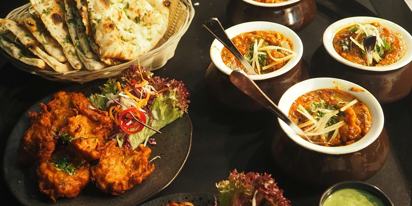 A mouth-watering view of table served with different cooked dishes and flatbreads.