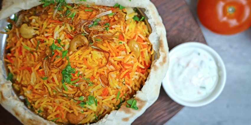 A mouth-watering view of a pot served with cooked rice garnished with onions and cashews.