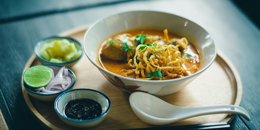 A mouth-watering view of a bowl of ramen with a few dips on the side on a table.