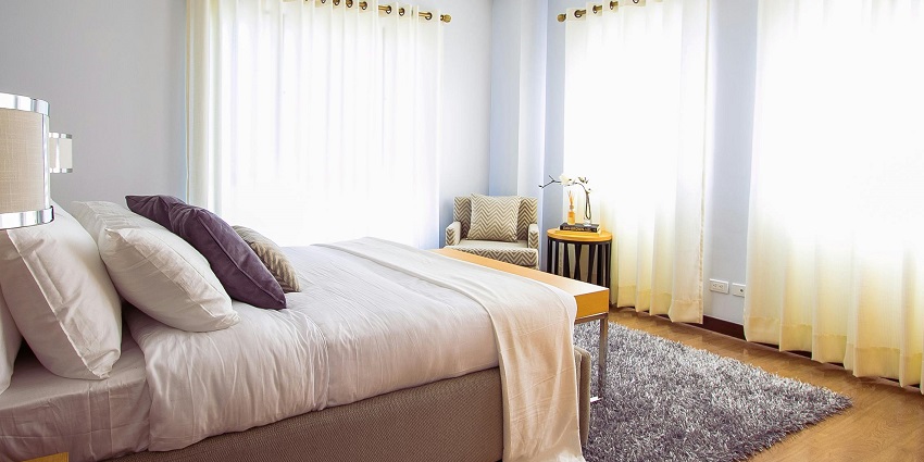 A breathtaking view of a bedroom with a bed and a side table with lamps and windows.