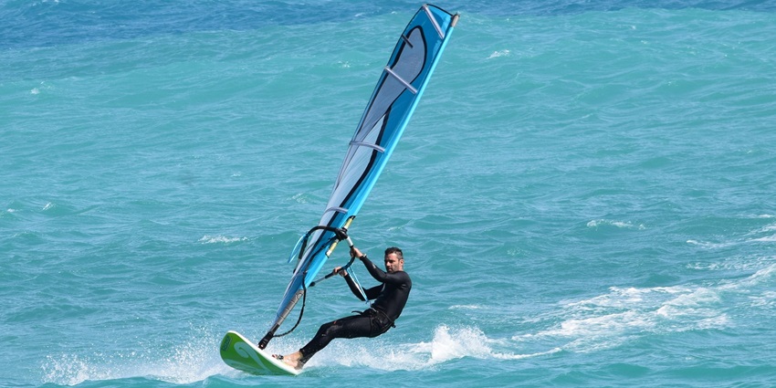 A person seen enjoying windsurfing in a vast water body on a sunny day