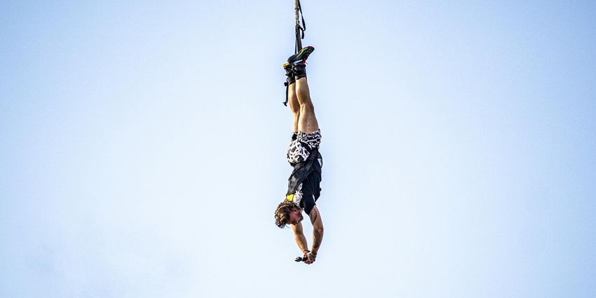 A man hanging from a rope during a bungee jump, with a scenic view of sky in the background.