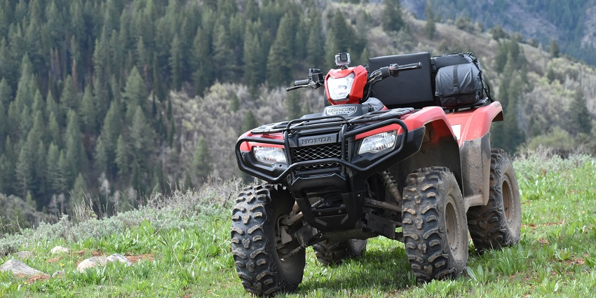 A mesmerising view of a red ATV ride on a grassy hill with mountains in the background.