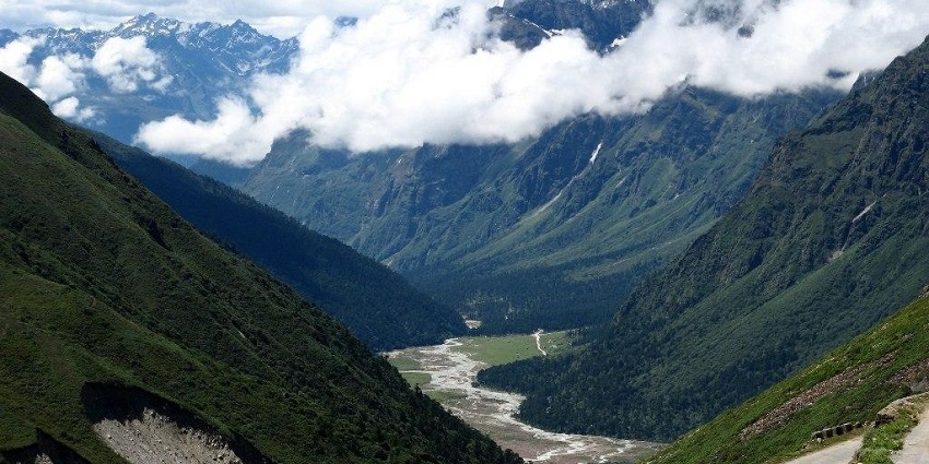 Trek route with high mountains, trees, and rocky area in Yumthang Valley in April.