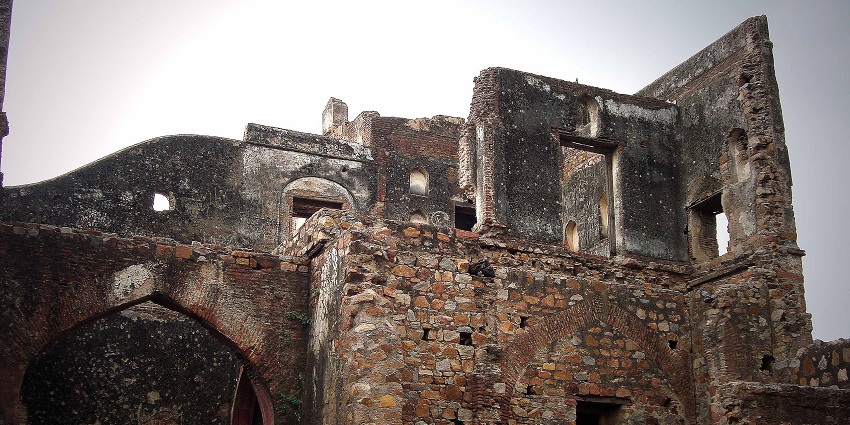 Weathered stone ruins of an ancient fort, with arched doorways and window openings