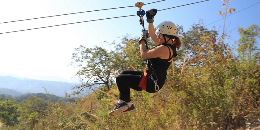 A stunning view of a woman enjoying zip lining above lush green meadows in the day.