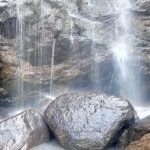 Water cascading from a height and dropping down at the rocks, providing a scenic view.